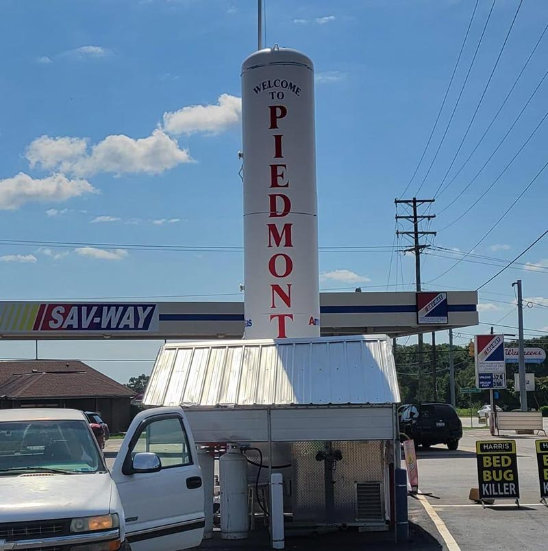 A tank on which it is written Welcome to Piedmont and at the back there is a gas station.